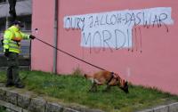 Ein Polizist mit einem Fährtenhund sucht vor eine Hauswand mit dem Schriftzug «Oury Jalloh - Das war Mord» nach Spuren