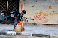 Anmerkung zum Bild: Ein Mädchen trägt einen Wasserkanister in Yarmouk, dahinter die Wandparole "Wir spucken auf alle palästinensischen Fraktionen."