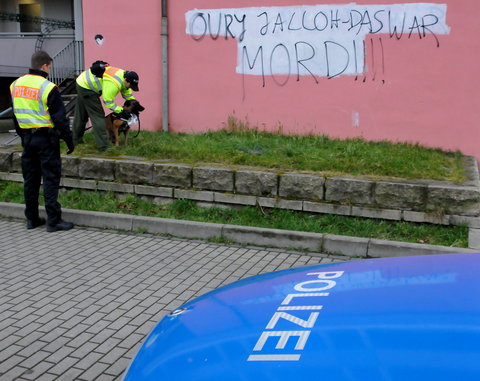 Zwei Polizisten mit einem Fährtenhund sucht vor eine Hauswand mit dem Schriftzug «Oury Jalloh - Das war Mord» nach Spuren