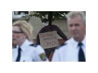 Polizeibeamte stehen vor einer Stoffpuppe, die ein Schild mit der Aufschrift "Denkt noch jemand an die Opfer?" trägt
