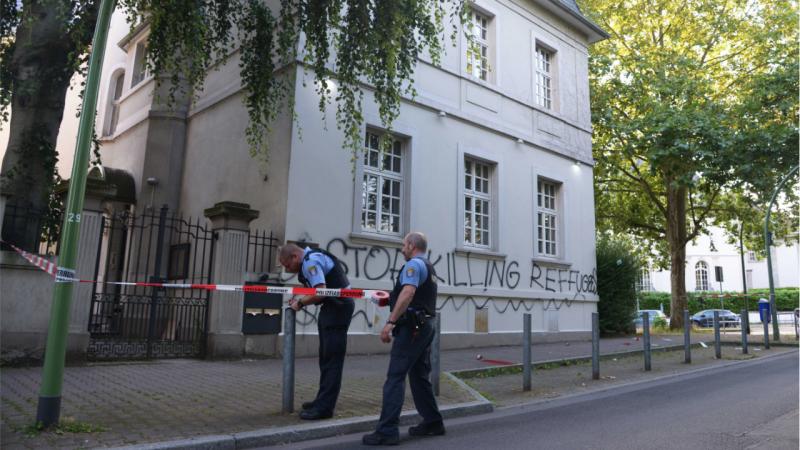 Polizisten sichern das Konsulat nach der Attacke ab. Im Hintergrund der Schriftzug „STOP KILLING REFFUGEES" mit Rechtschreibfehler