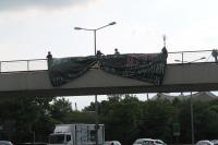 Aktivist*innen hängen ein Transparent an einer Brücke im Olympiapark München auf.