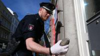 Der Polizist hebt die Steine auf, womit die Chaoten wahrscheinlich auf die Filiale warfen