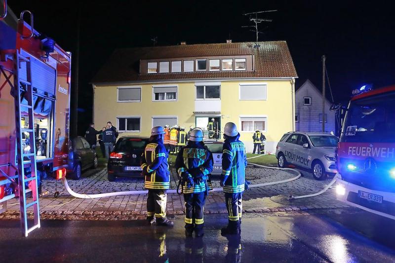 Einsatzkräfte der Feuerwehr stehen vor dem Haus, in dem das Feuer gelegt worden ist.