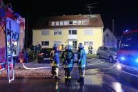 Einsatzkräfte der Feuerwehr stehen vor dem Haus, in dem das Feuer gelegt worden ist.